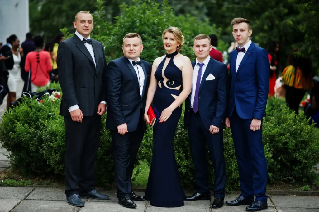 A student group in a Tuxedo and gown smiling with friends during prom photos