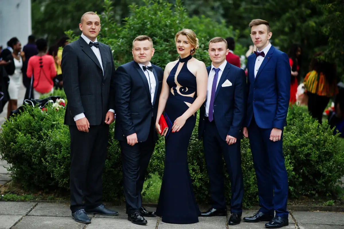 A student group in a Tuxedo and gown smiling with friends during prom photos
